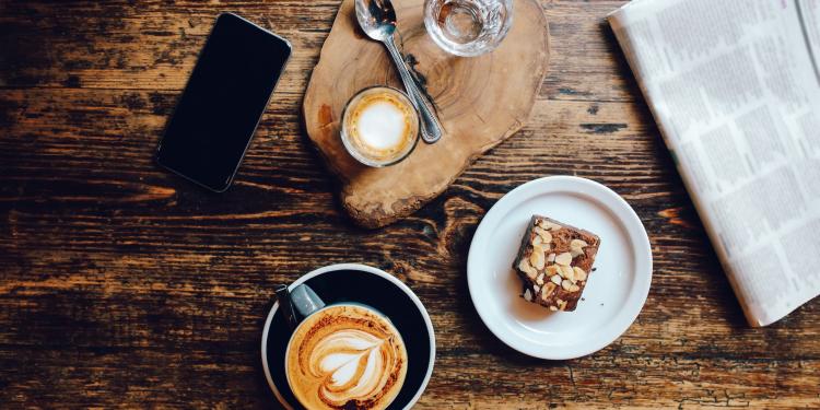 A newspaper with coffee, cake and mobile phone