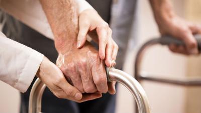 man with mobility issues receiving assistance walking with frame